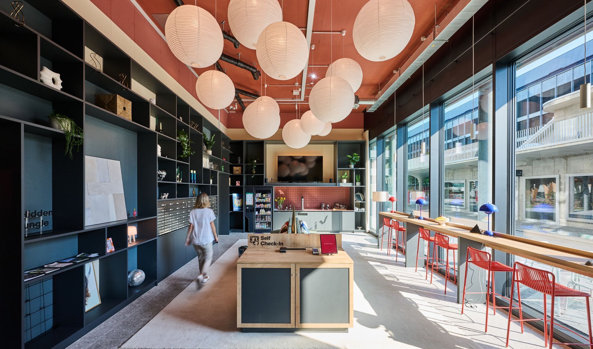 Modern café interior with hanging lanterns, red stools, and large windows overlooking the street.