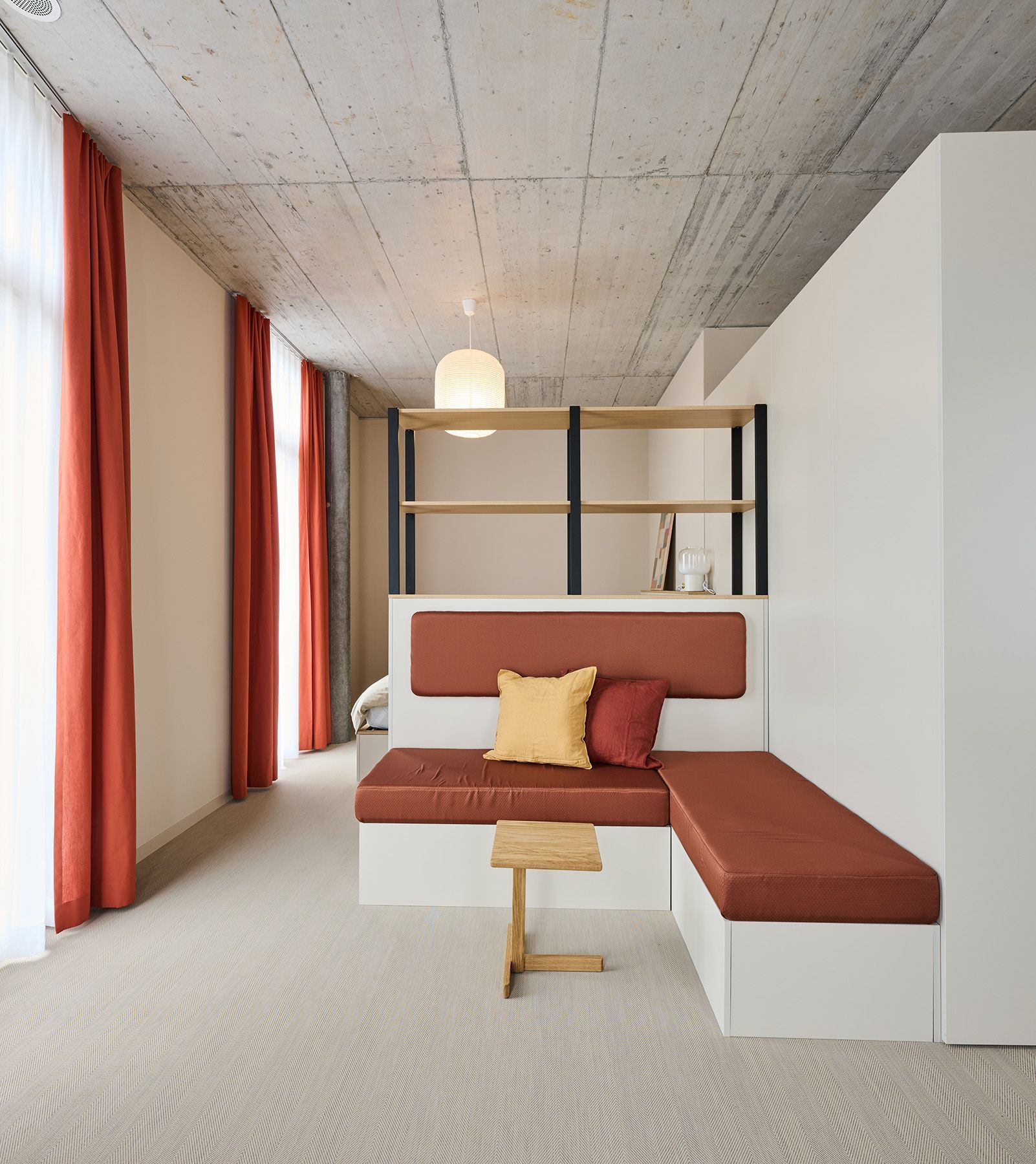 Modern minimalist living room with red-orange curtains, built-in bench seating, and a concrete ceiling