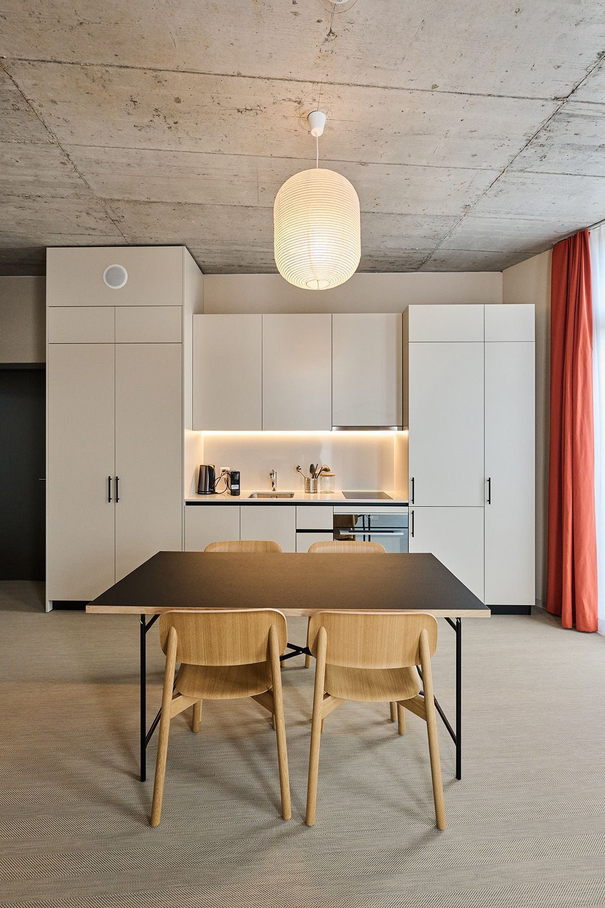 Modern kitchen with white cabinets, wood table and chairs, pendant light, and red curtains