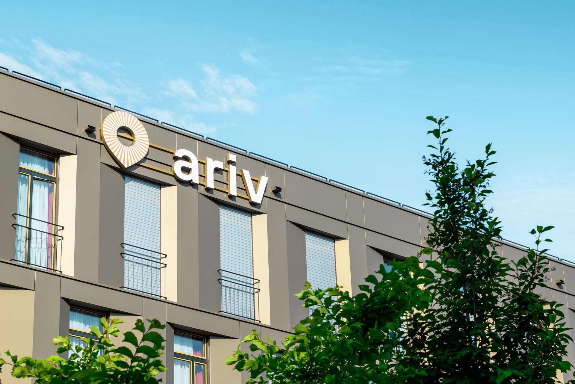 Modern building facade with ariv sign and trees against a blue sky