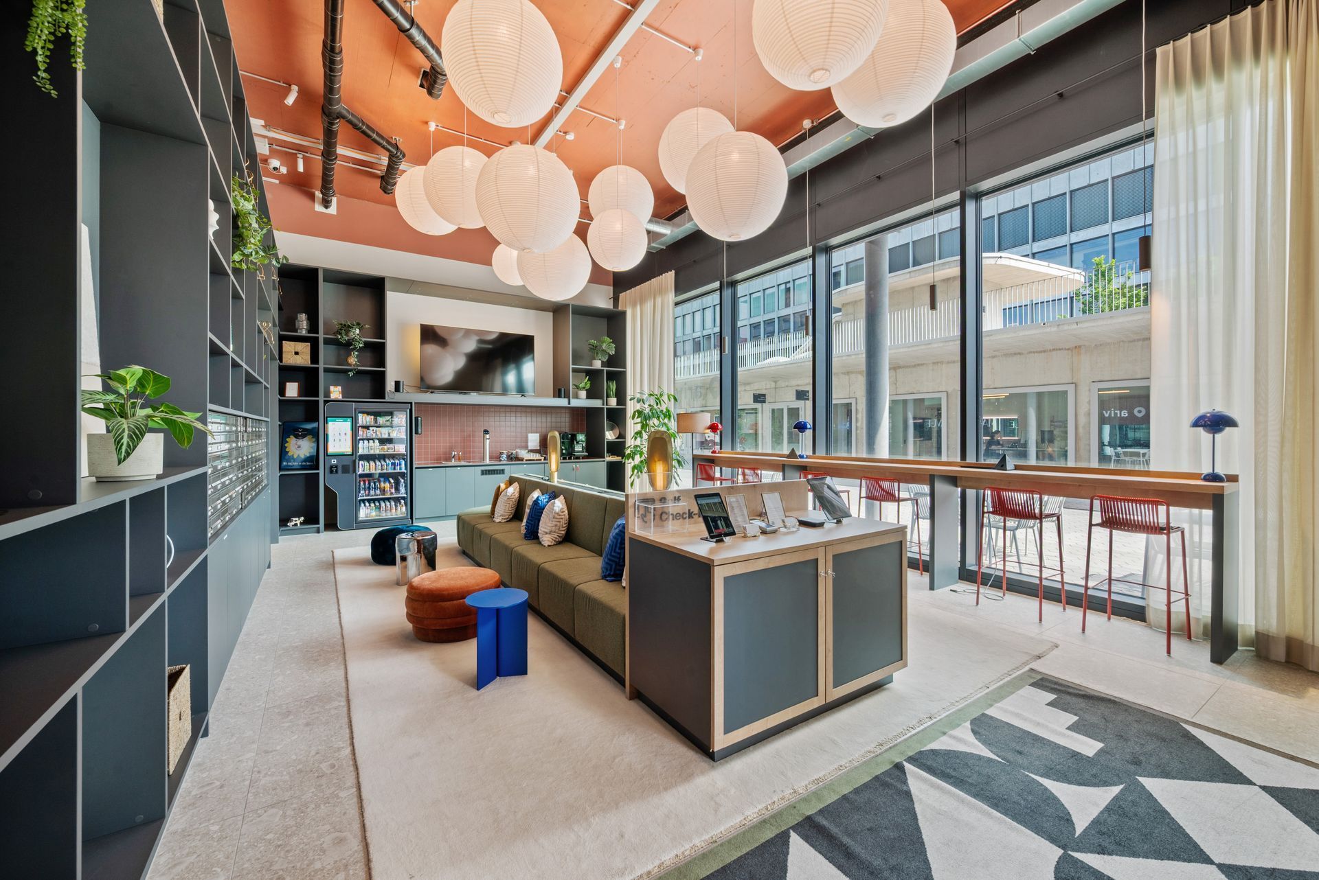 Modern office lounge with sofas, pendant lights, and floor-to-ceiling windows overlooking a city street