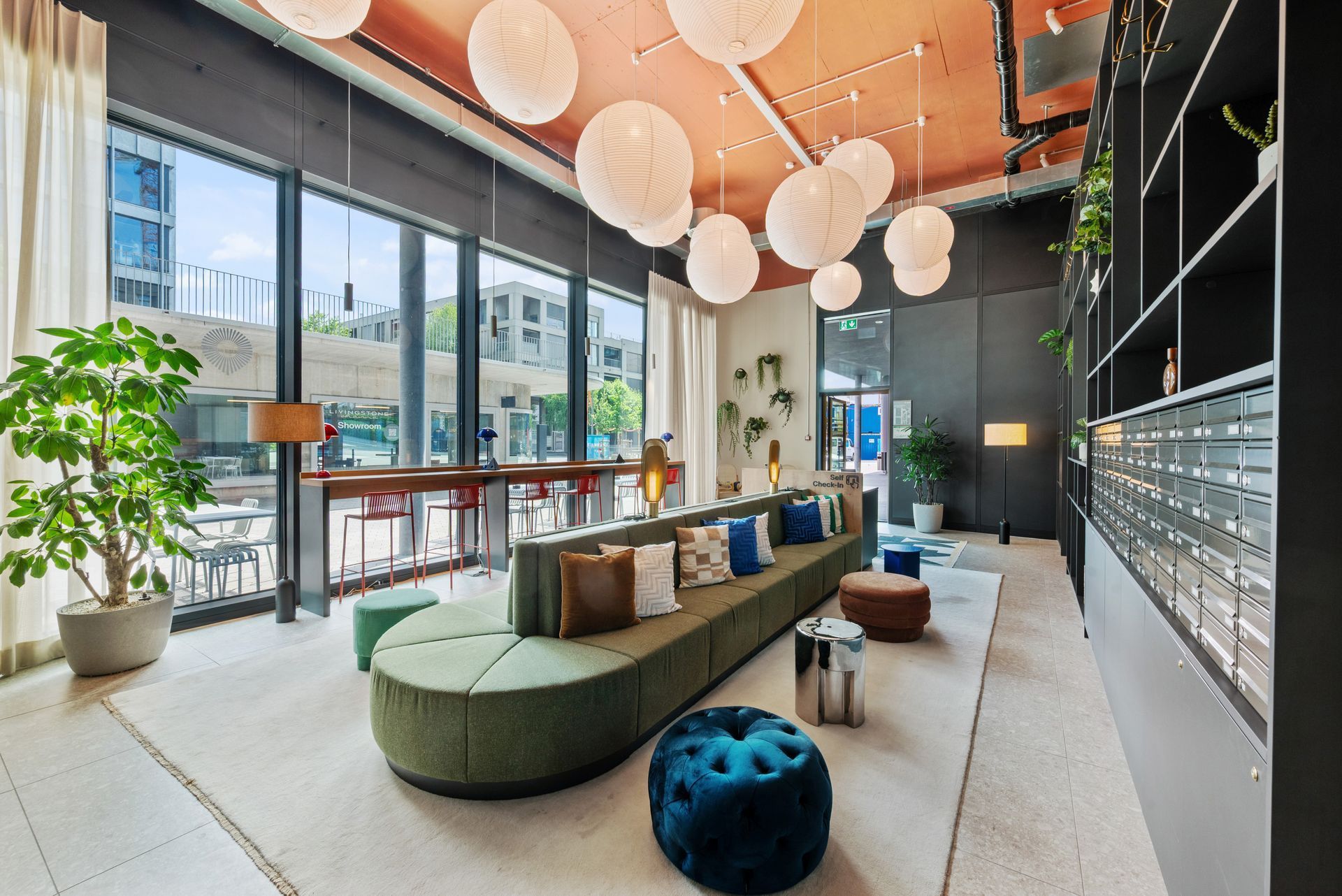 Modern lounge with green curved sofa, hanging globe lights, large windows, and potted plants