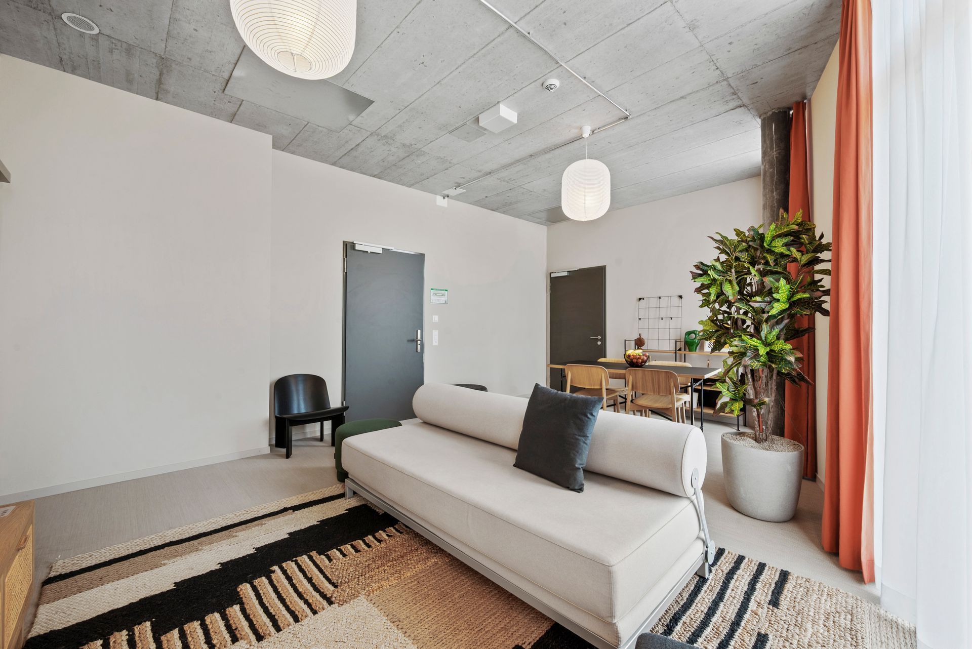 Modern living room with white sofa, black chair, potted plant, and large orange curtains