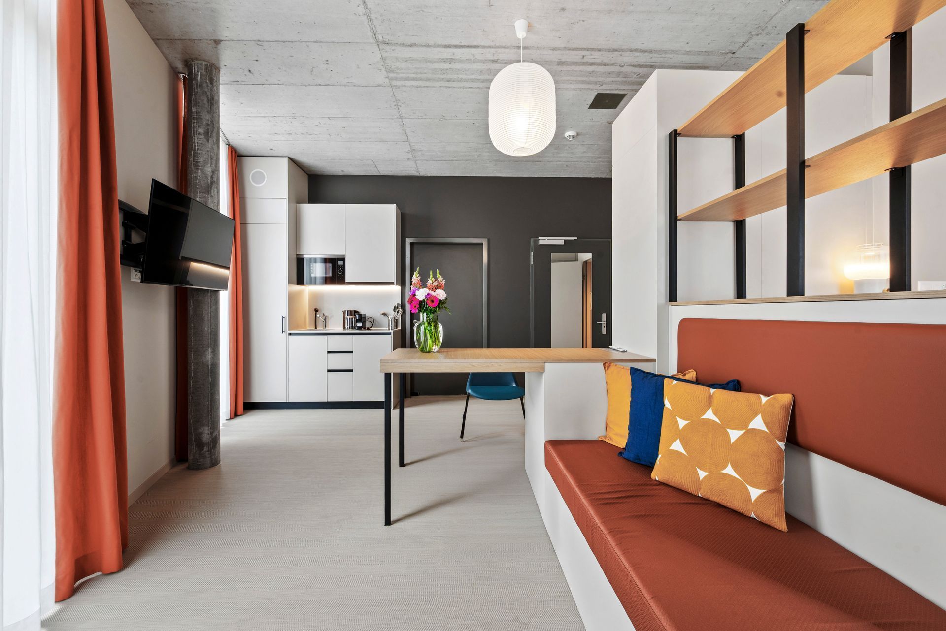 Modern studio apartment with orange sofa, desk, kitchenette, and large windows