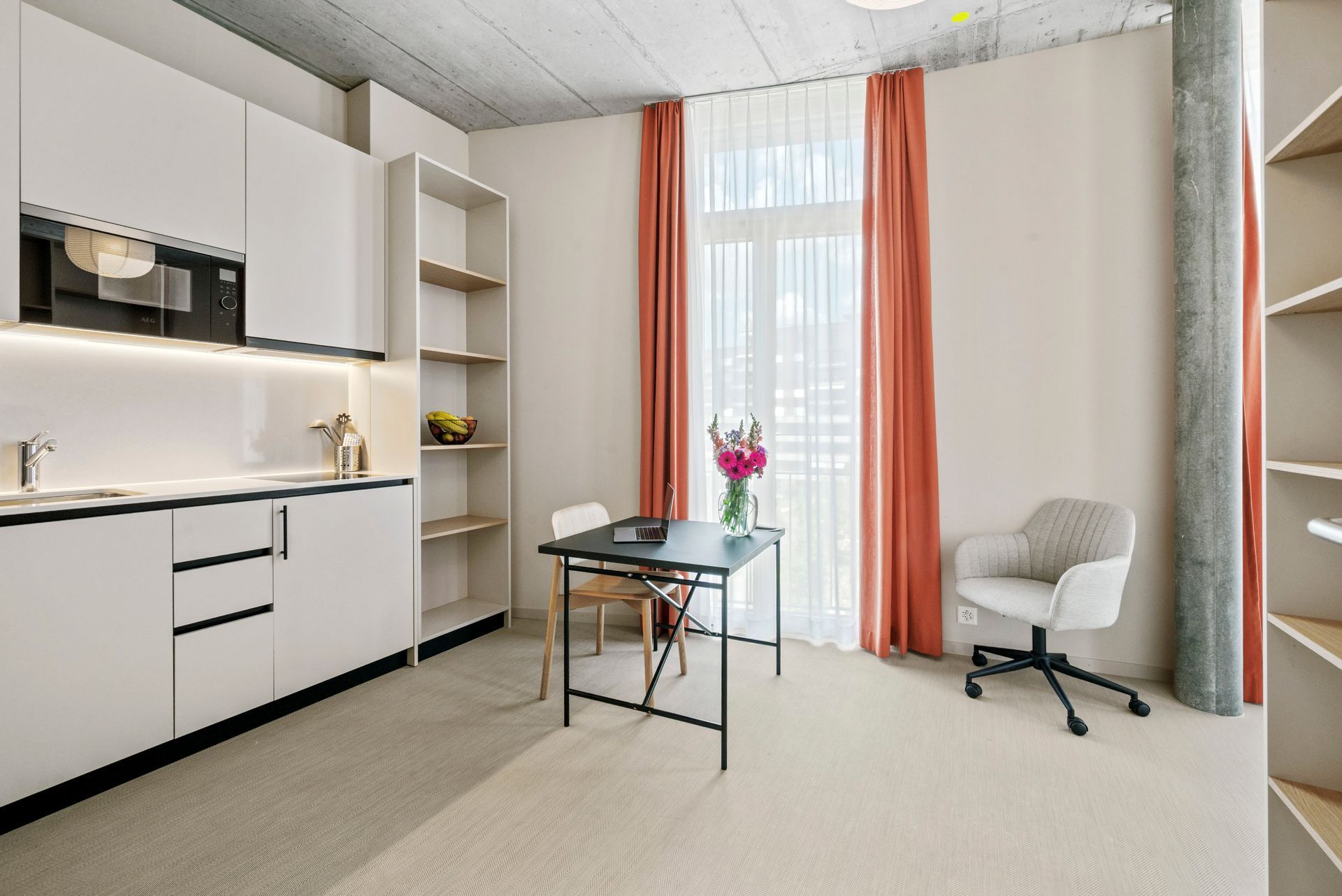 Bright modern room with white cabinetry, glass table, armchair, and coral curtains by a window.