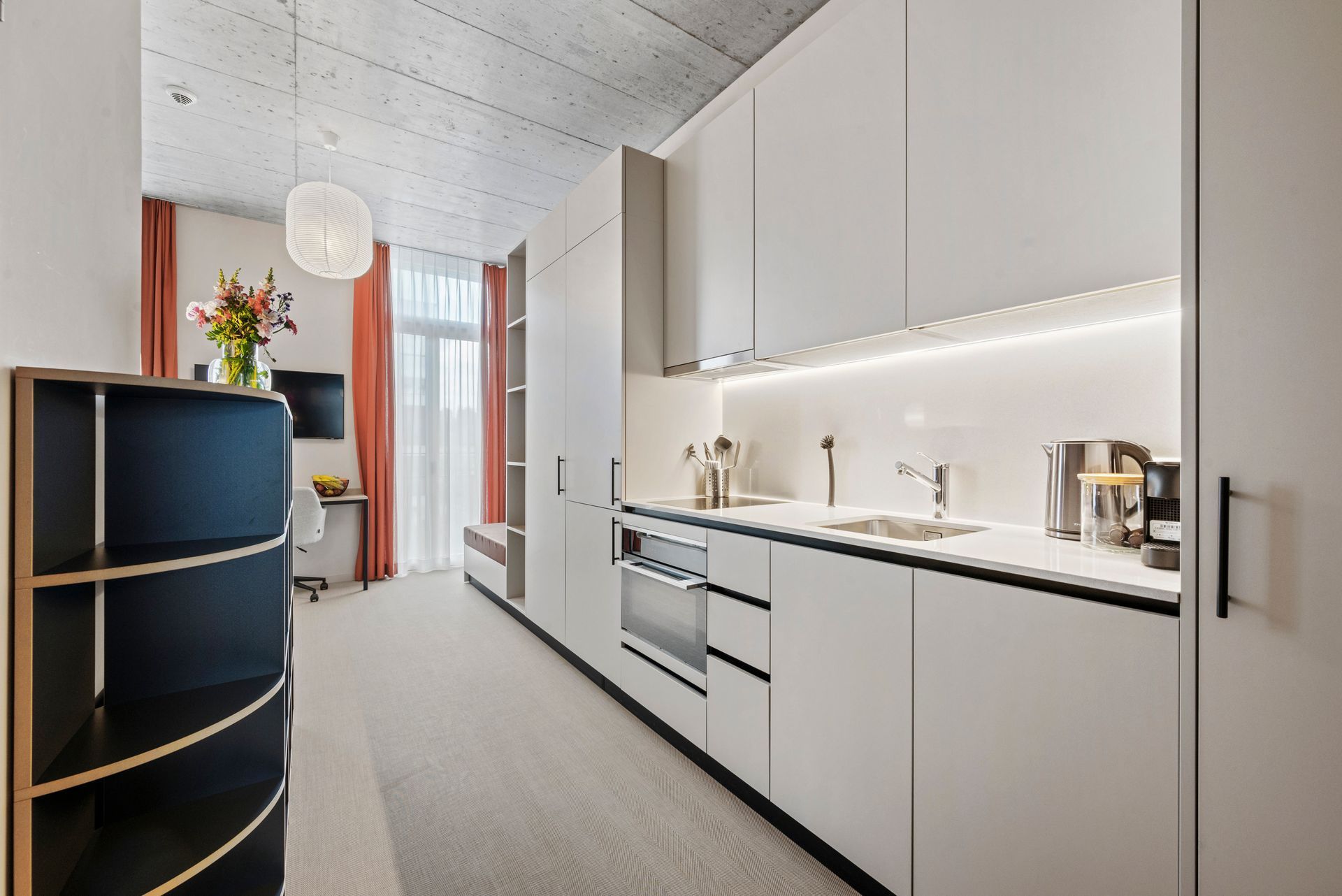 Modern minimalist kitchen hallway with white cabinets, black countertop, and a narrow dining nook with orange curtains