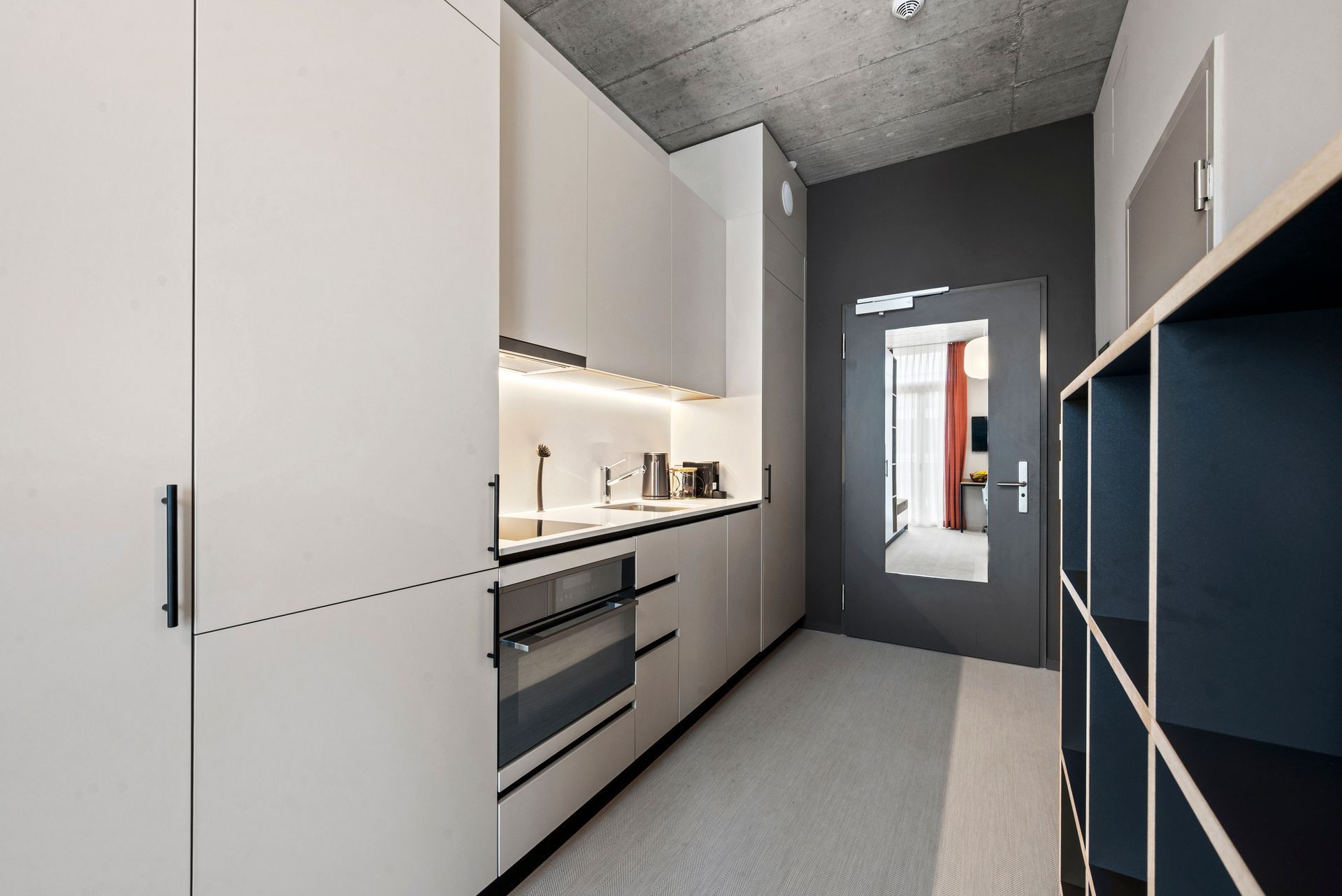 Modern galley kitchen with white cabinets, built-in oven, and dark accent wall