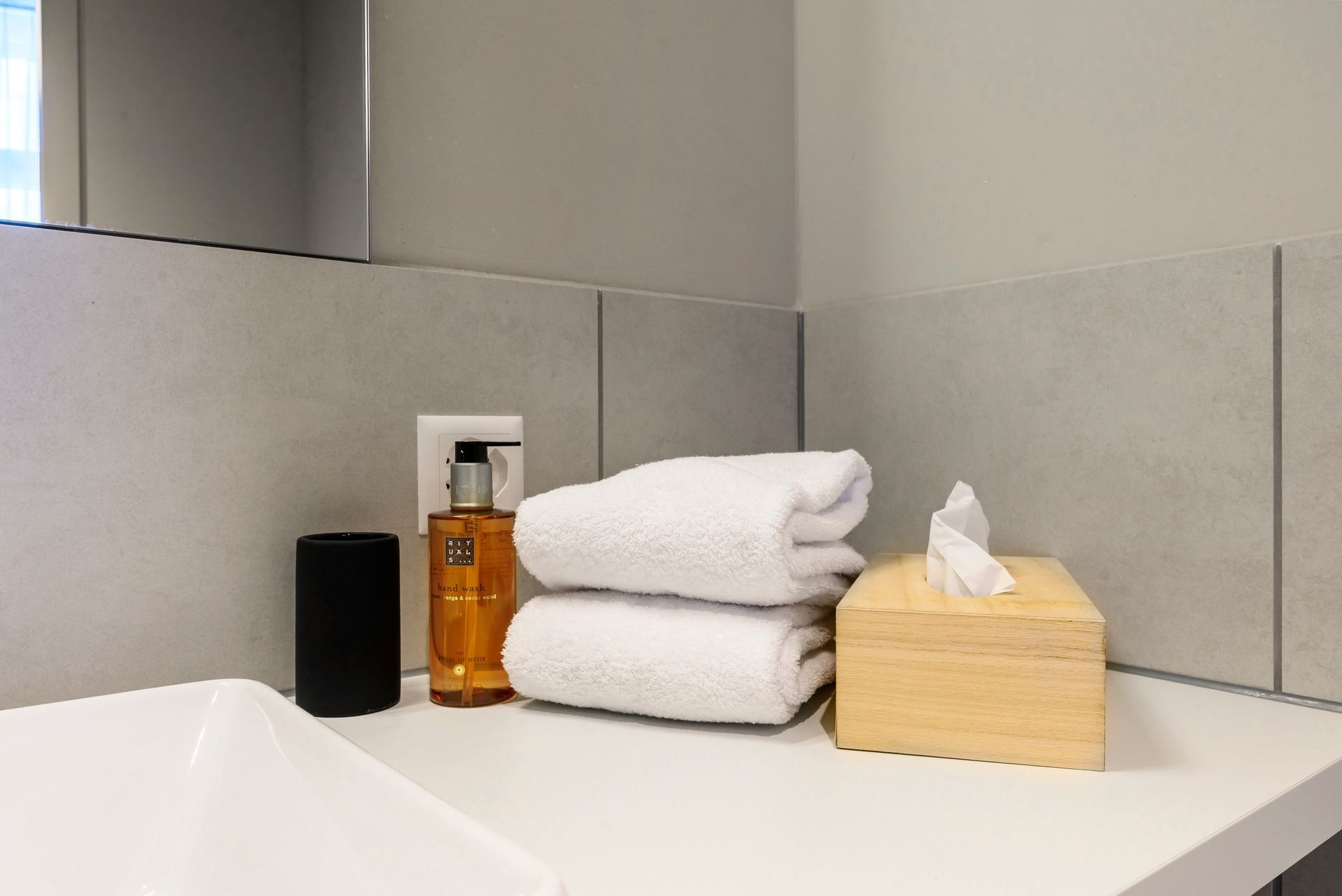 Bathroom countertop with folded white towels, amber soap bottles, and a tissue box by the sink.