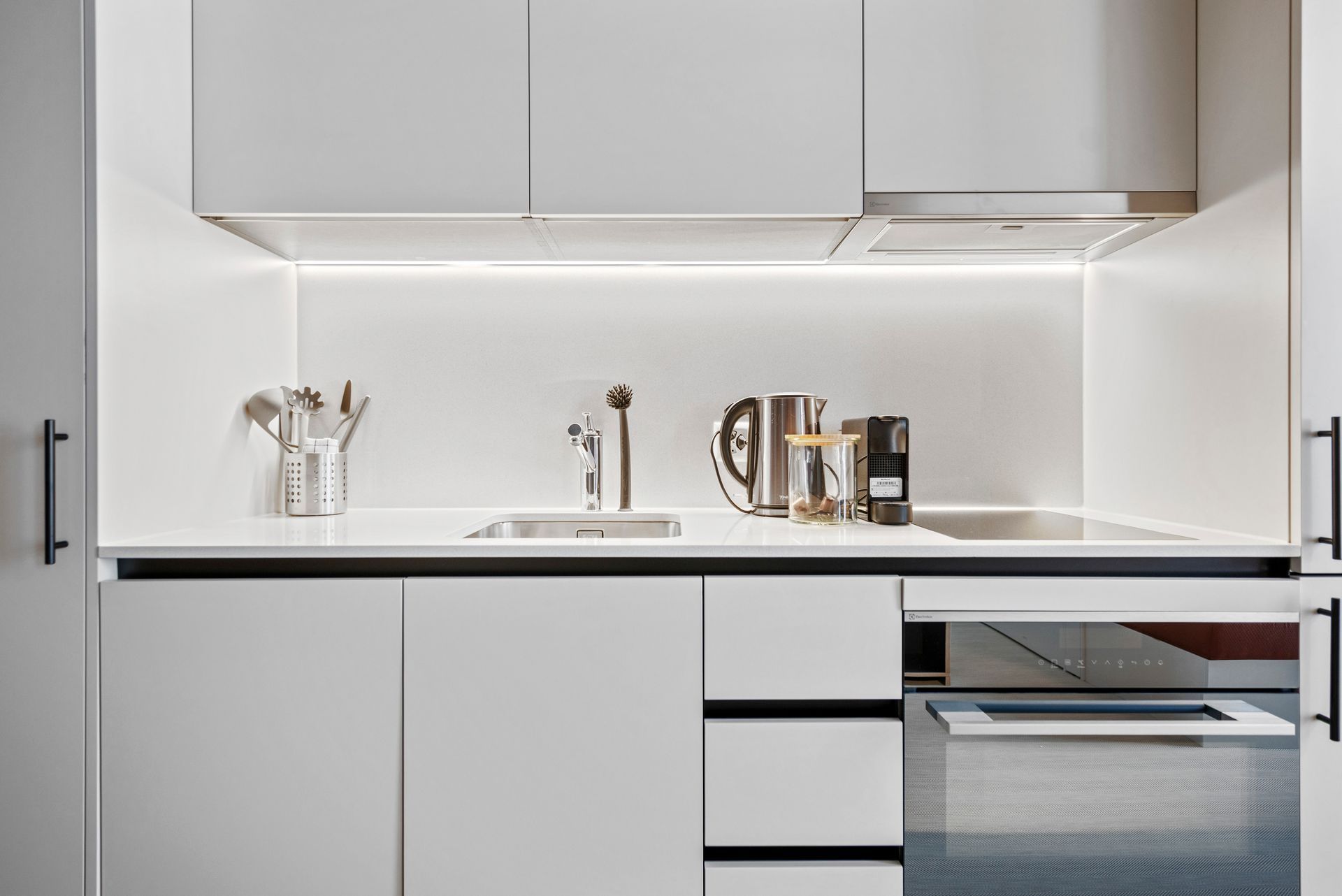 Modern white kitchen with sleek cabinets, countertop sink, and stainless steel kettle and toaster