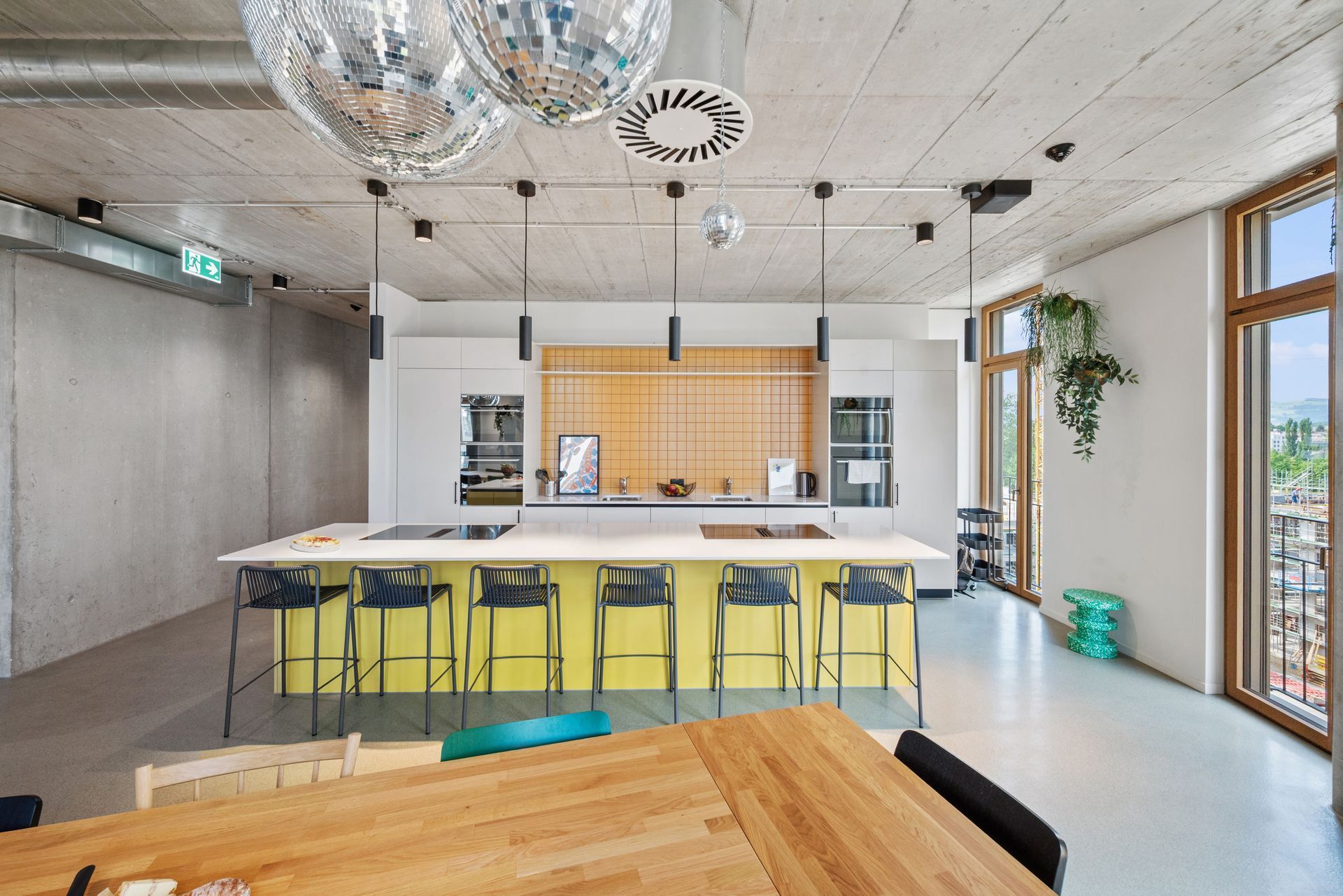 Modern kitchen with yellow island, bar stools, and large windows in a bright open room