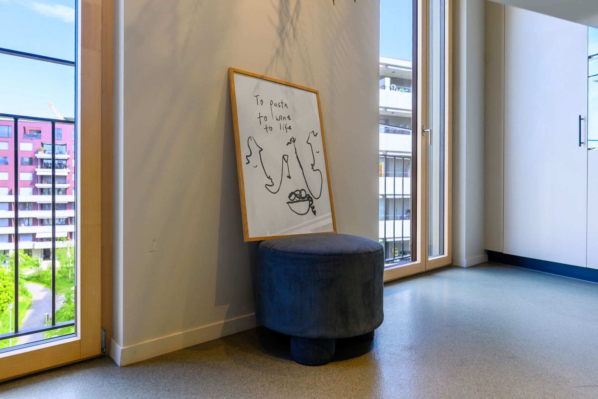Lobby corner with whiteboard on a dark ottoman beside a window and bright hallway wall