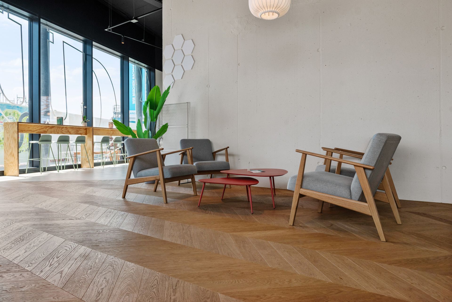 Modern lounge with wooden chairs, red table, and large windows in a bright, minimalist room