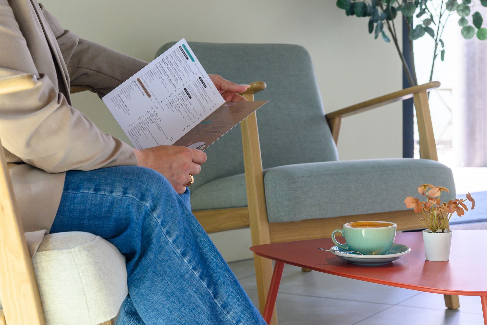 Person reading a magazine on a sofa beside a coffee table with a cup and small flower vase