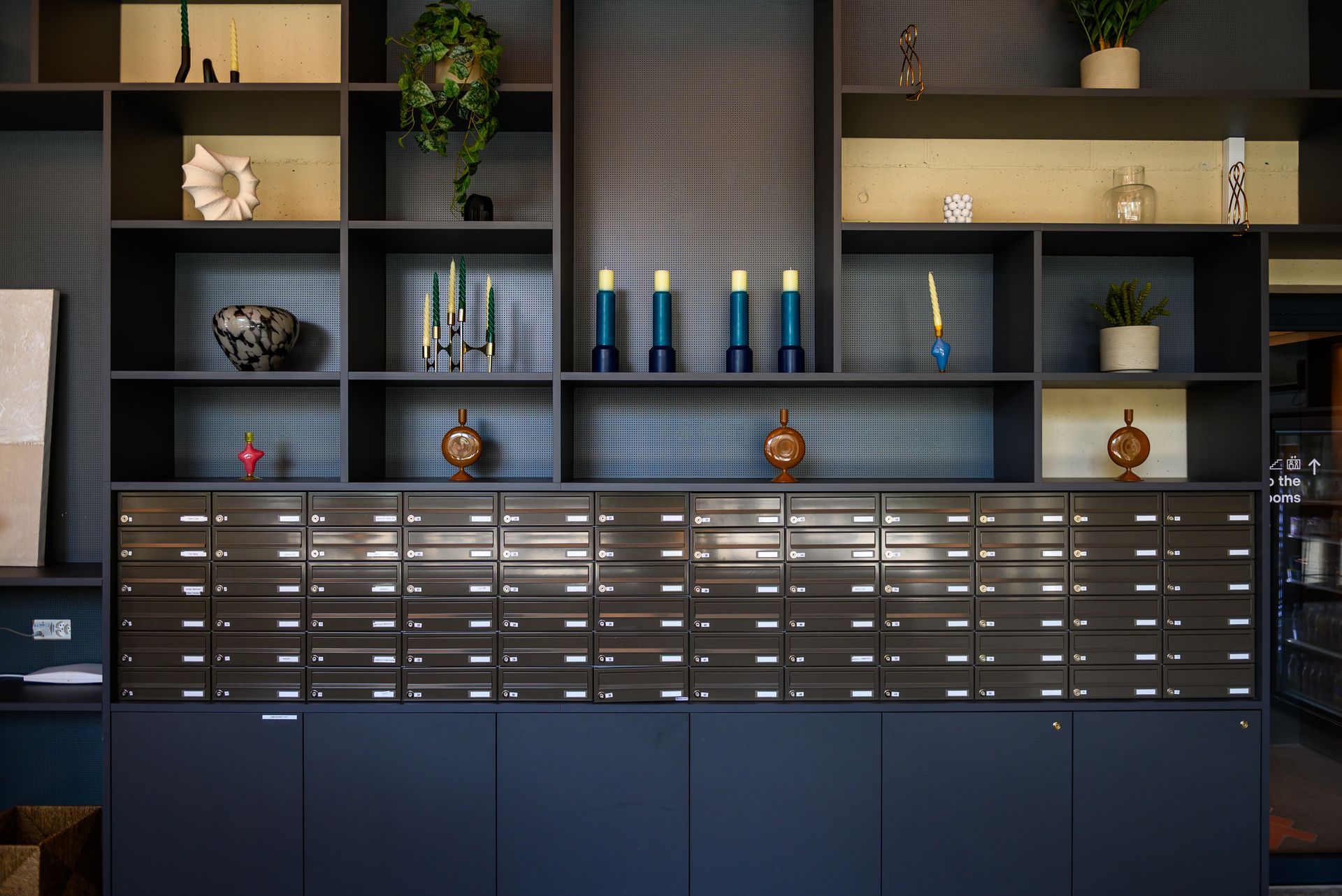 Modern office shelving with plants, books, awards, and blue cabinets beneath a tiled wall