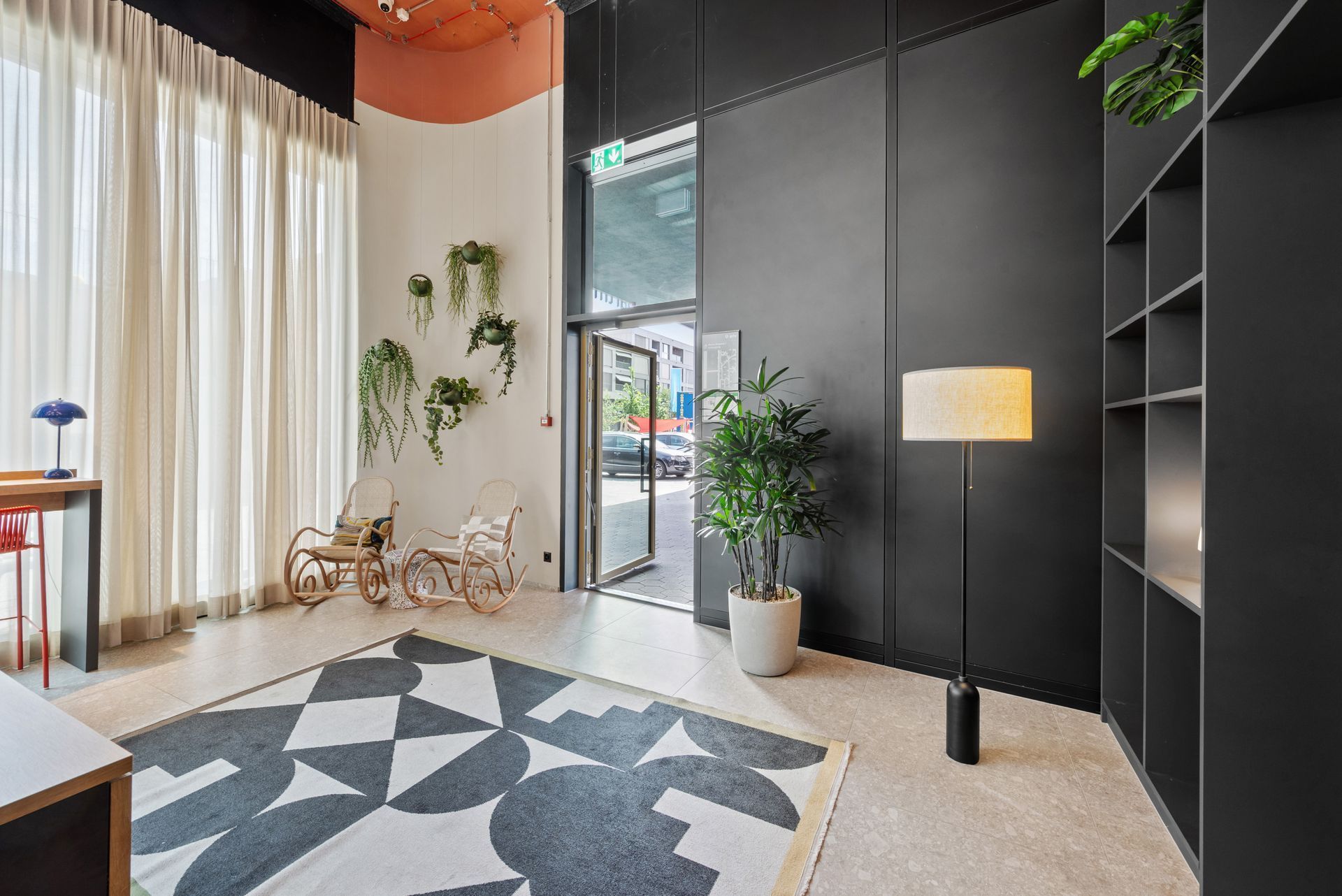 Modern lobby with geometric rug, black wall panels, potted plants, and floor lamp by large windows