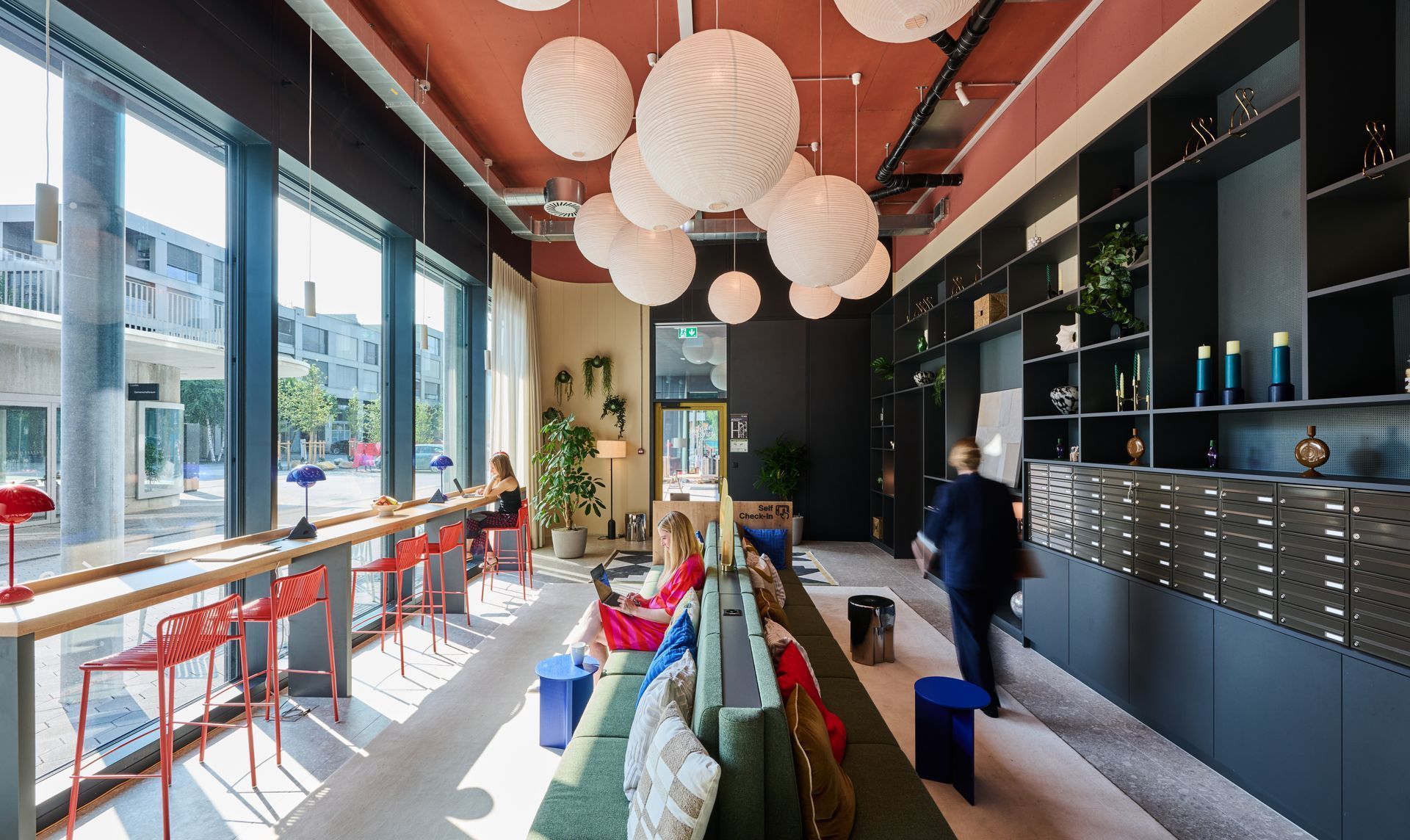 Modern café interior with hanging globe lights, long windows, and a person near the counter.