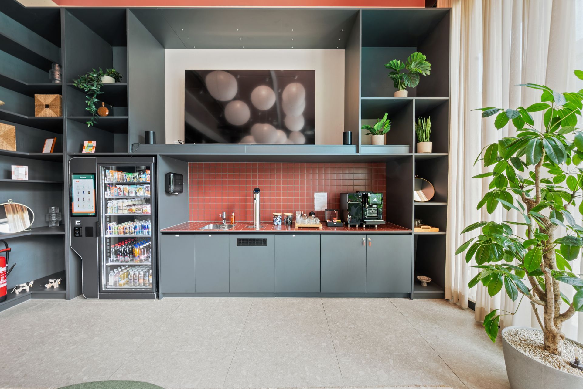 Modern kitchenette with gray cabinets, red tile backsplash, mini fridge, shelves, and a plant by a window
