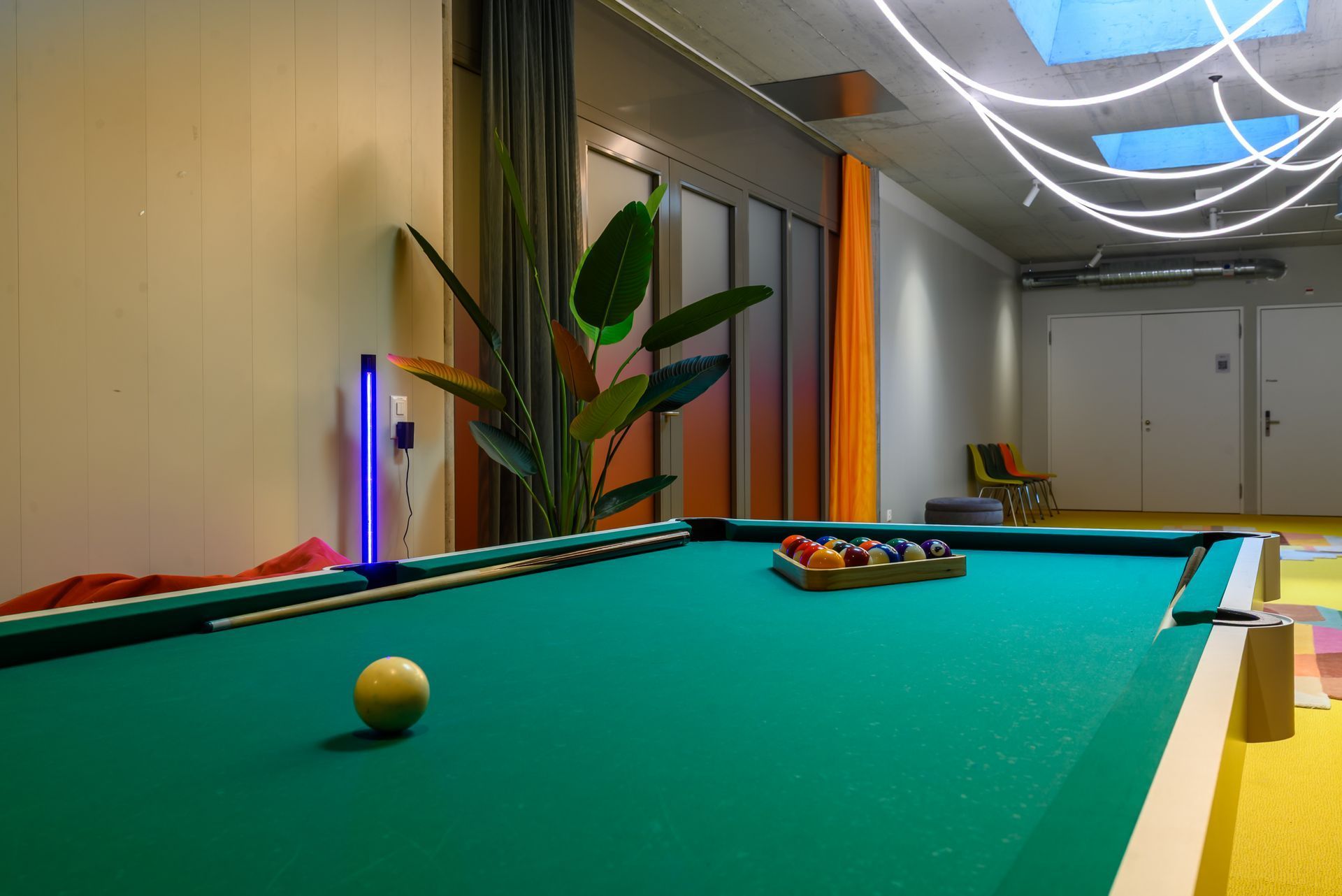 Pool table in a modern room with a single cue ball and a rack of balls near the far end.