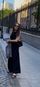 Woman standing on a city sidewalk beside a black railing, holding a bag and looking at her phone.