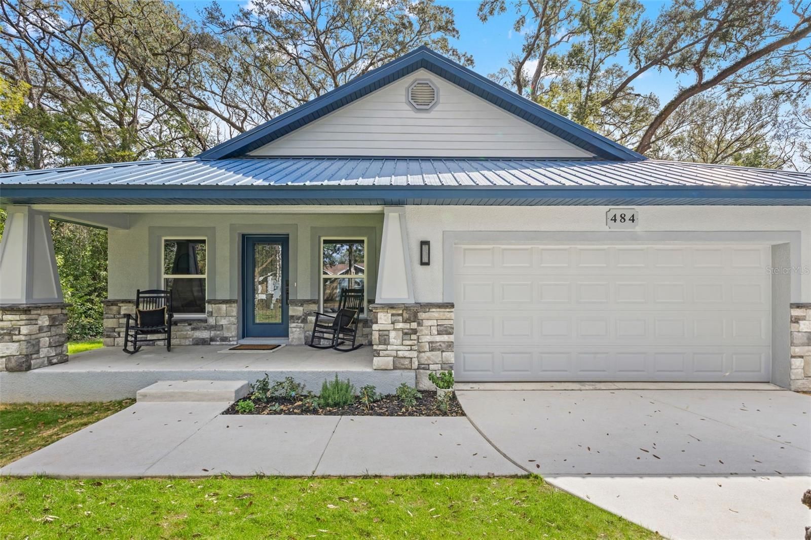 Blue-trimmed single-story house with a front porch, two chairs, and a two-car garage