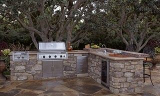 An outdoor kitchen with a grill , sink , and trees in the background.