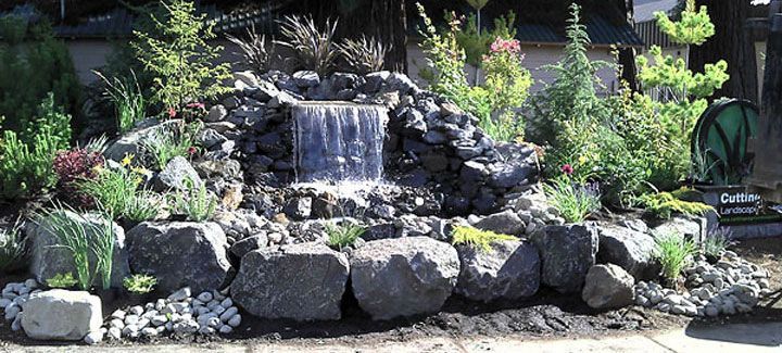 A waterfall is surrounded by rocks and plants in a garden.