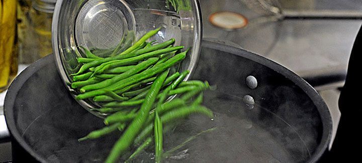 Green beans are being poured into a pot of boiling water.