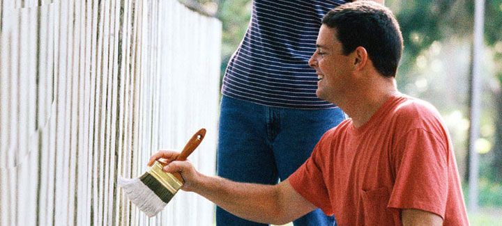 A man is painting a white fence with a brush.
