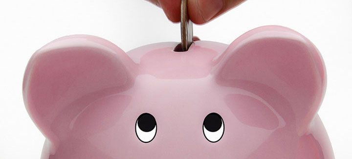 A person is putting a coin into a pink piggy bank.
