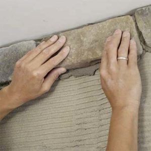 A person is installing a stone fireplace on a wall.