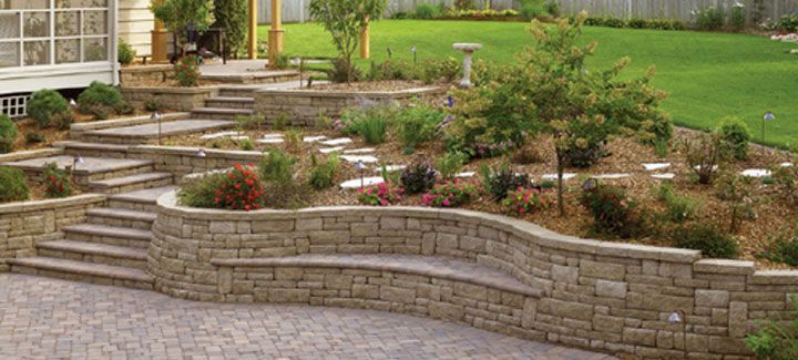 A stone wall with stairs leading up to a lush green yard.