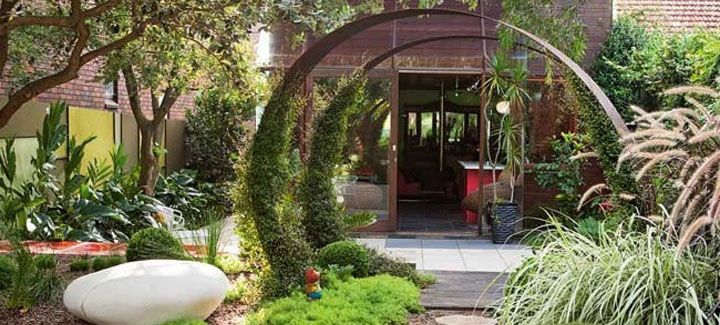 A garden with a large archway leading to a house.