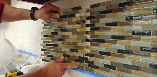 A man is installing a tile wall in a kitchen.