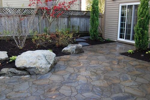 A stone patio in front of a house with a fence in the background