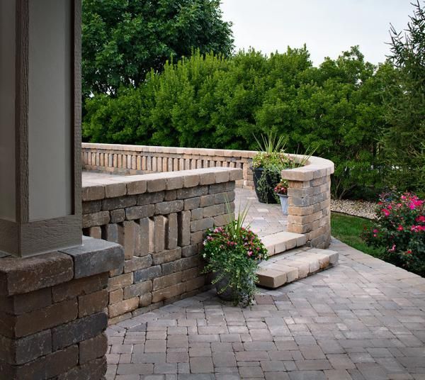 A brick patio with steps leading up to a brick wall and trees in the background.