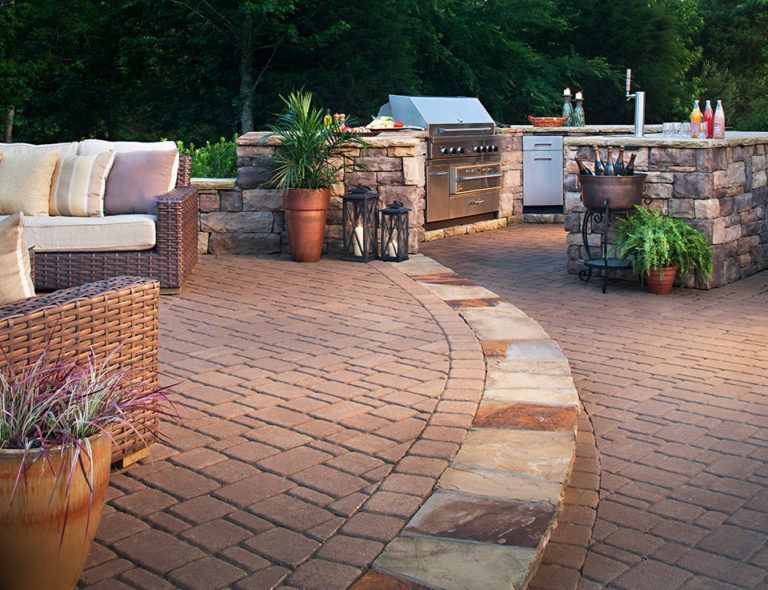 A patio with a couch , chairs , lanterns and a grill.