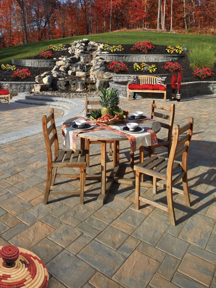 A table and chairs on a patio with a waterfall in the background.
