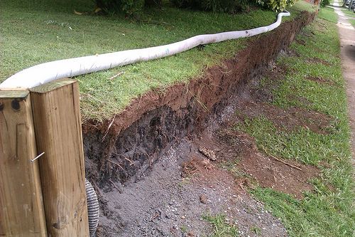 A hose is laying on the side of a dirt road next to a wooden post.