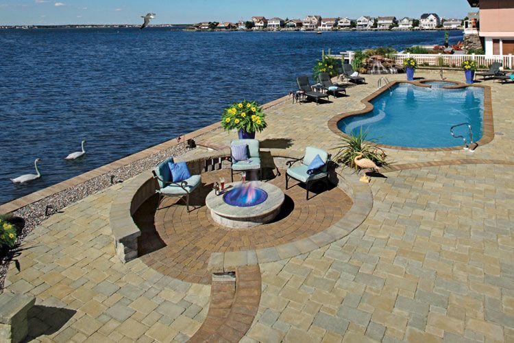A patio with a fire pit and a swimming pool next to a body of water.