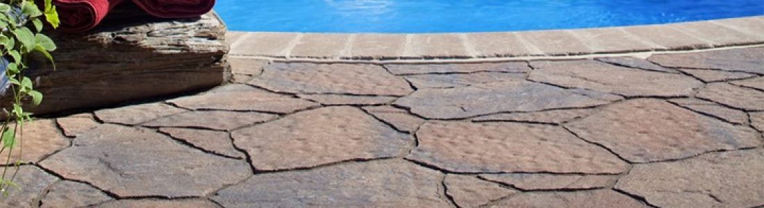 A brick patio next to a swimming pool with towels on a rock.