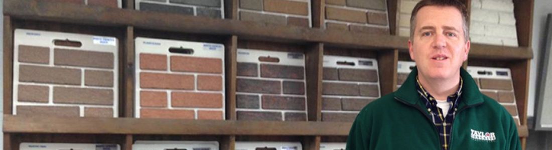 A man in a green jacket is standing in front of a brick wall.