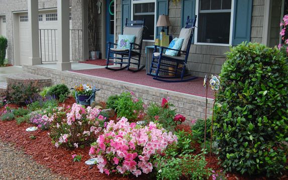 A porch with rocking chairs and flowers in front of a house.