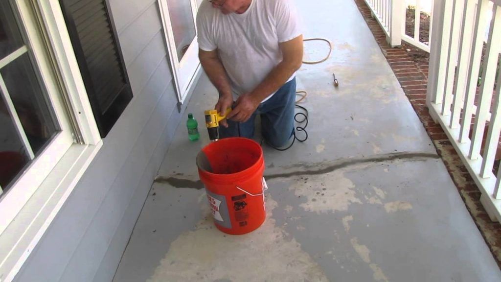 A man is kneeling down next to an orange bucket with a drill in it.