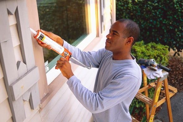 A man is applying caulk to a window on a house