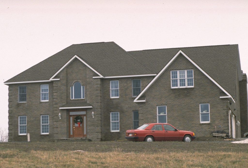 A red car is parked in front of a large brick house