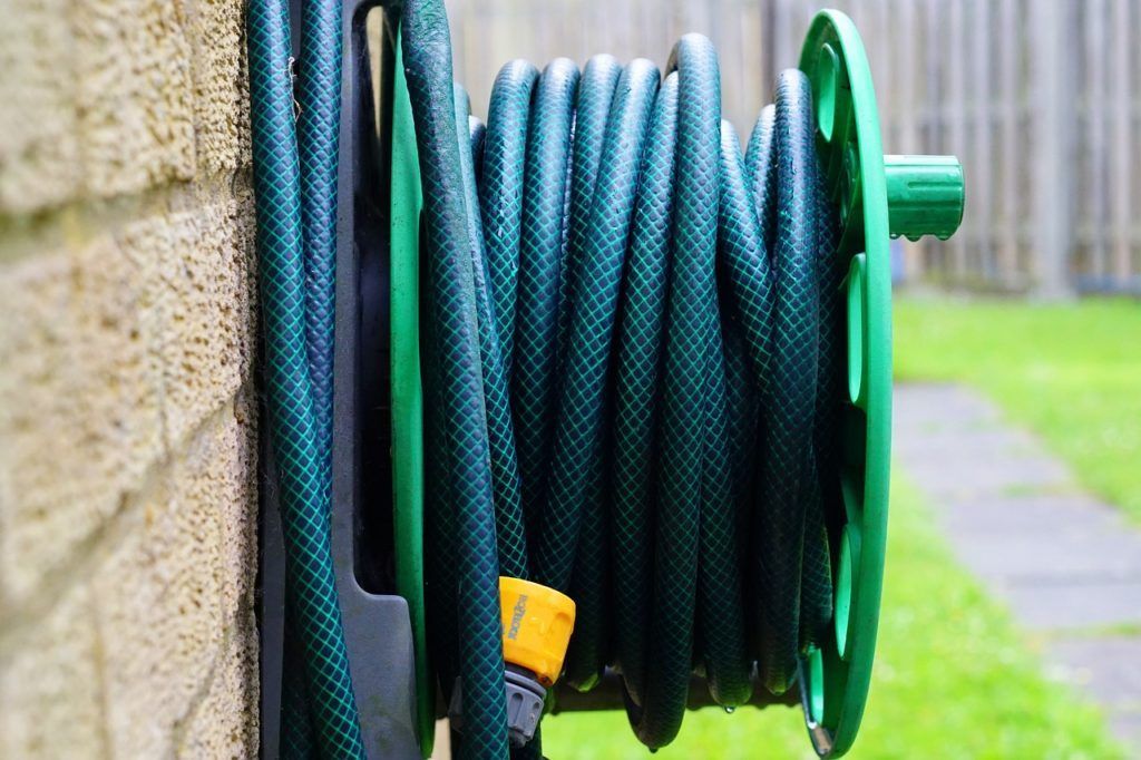 A green garden hose is hanging on a wall.