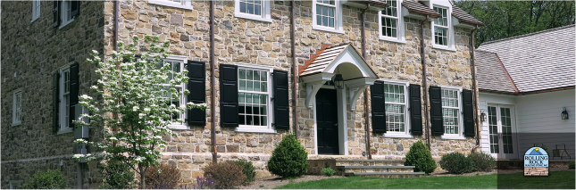 A large stone house with black shutters and a white awning