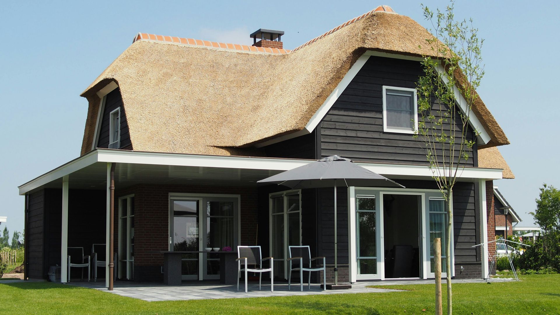 A black house with a thatched roof and a patio with chairs and umbrellas
