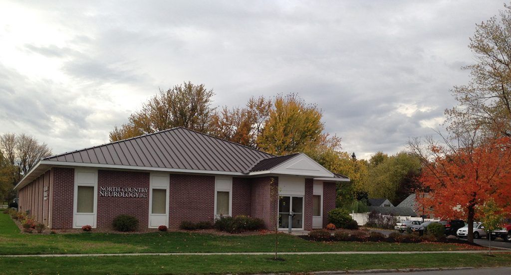 A brick building with a metal roof is surrounded by trees on a cloudy day