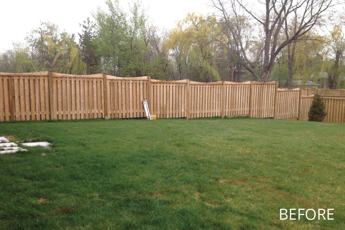 A backyard with a wooden fence and a lush green lawn.